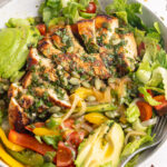 chicken fajita salad in a bowl with cilantro lime dressing on top and on the side.