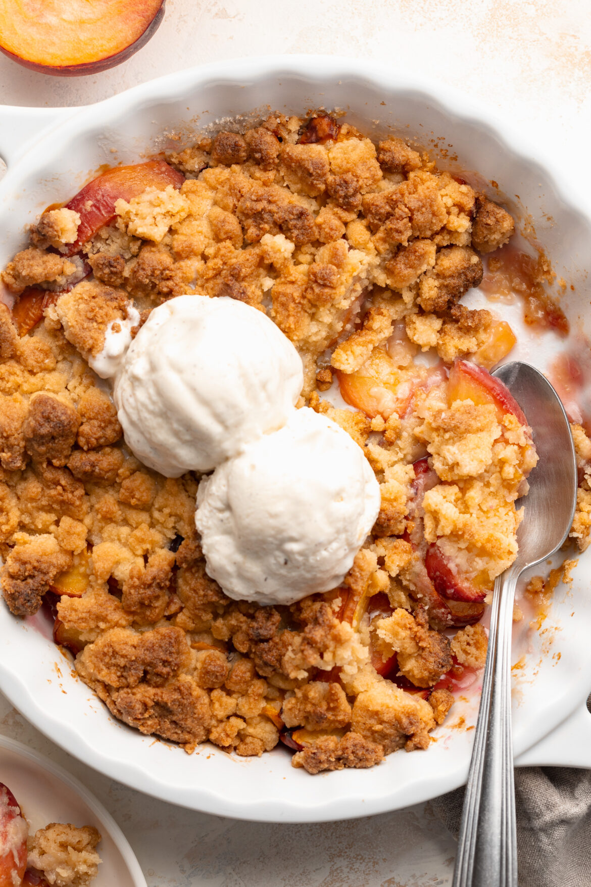 4 Ingredient Peach Cobbler (gluten-free!) overhead image of 4 ingredient peach cobbler in a baking dish with ice cream on top.