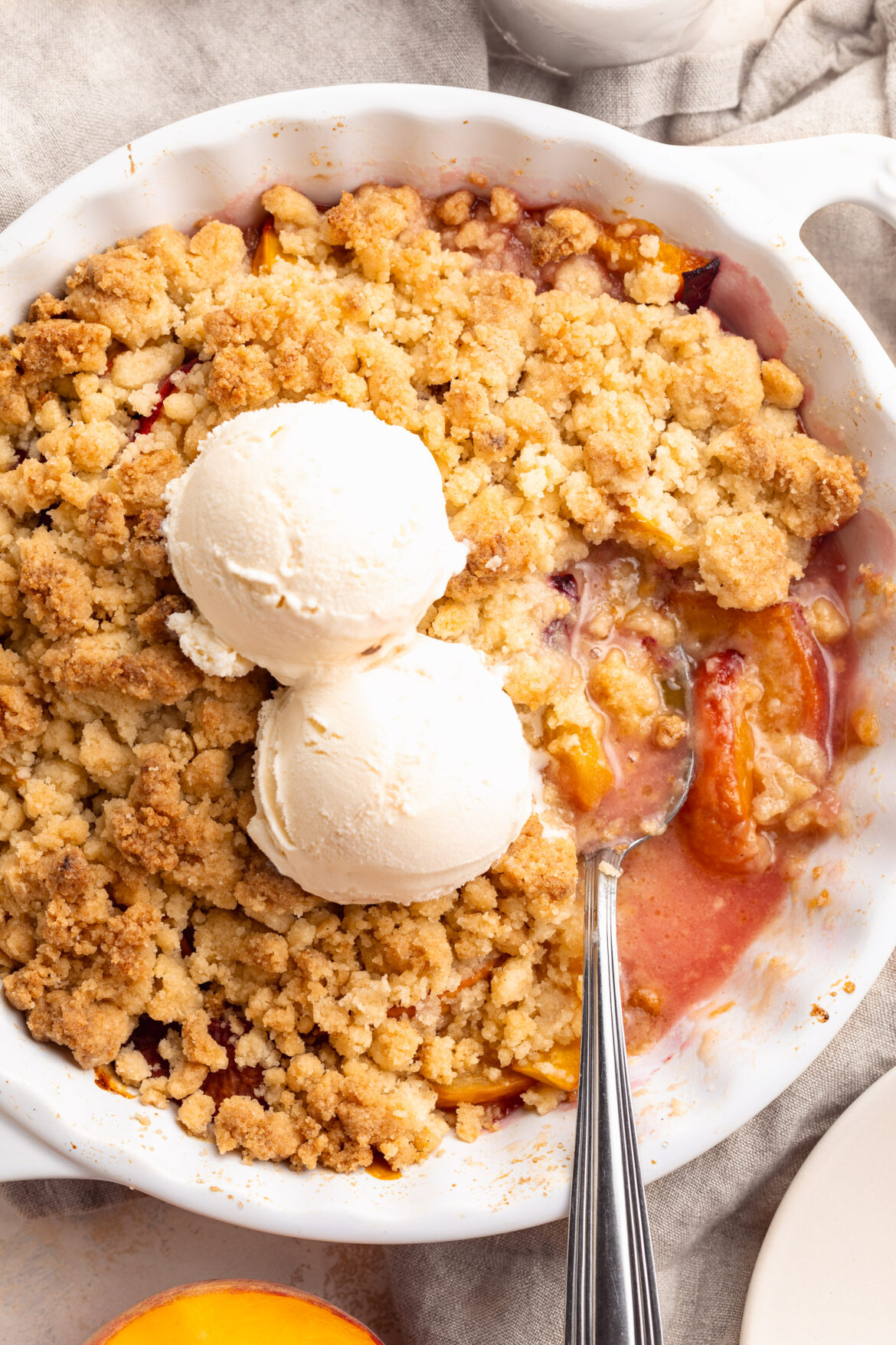 4 Ingredient Peach Cobbler (gluten-free!) 4 ingredient peach cobbler in a pie dish with two scoops of vanilla ice cream on top.