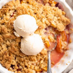 4 ingredient peach cobbler in a pie dish with two scoops of vanilla ice cream on top.