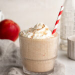 Apple pie protein smoothie in a glass with whipped cream and cinnamon on top.