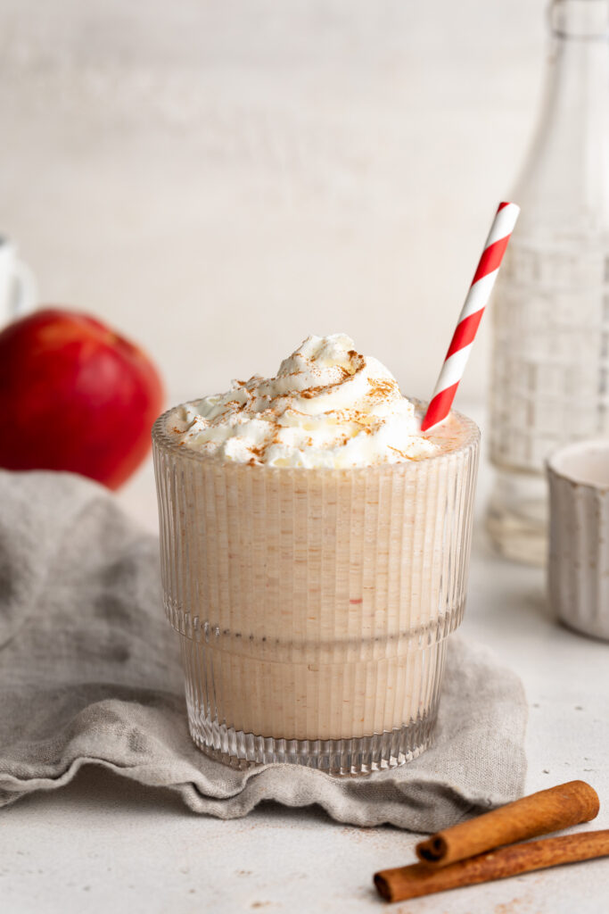 Apple pie protein smoothie in a glass with whipped cream and cinnamon on top.