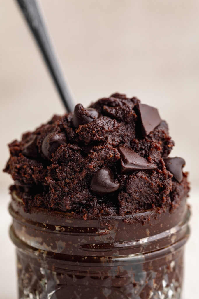 close up image of healthy edible brownie batter in a jar with a spoon.