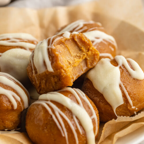 pumpkin protein balls on a plate with white chocolate drizzled on top.