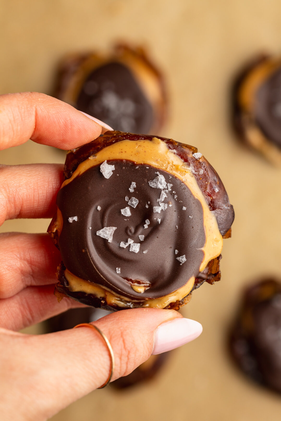 Smashed Dates with Peanut Butter and Chocolate hand holding a smashed date with peanut butter, chocolate, and flaky salt.