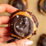 hand holding a smashed date with peanut butter, chocolate, and flaky salt.