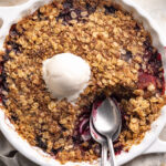 Overhead image of triple berry crisp with frozen berries in a baking dish with a scoop of vanilla ice cream on top.