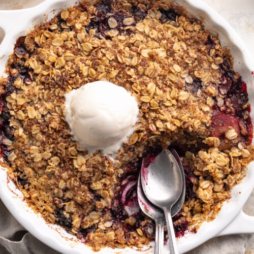Overhead image of triple berry crisp with frozen berries in a baking dish with a scoop of vanilla ice cream on top.