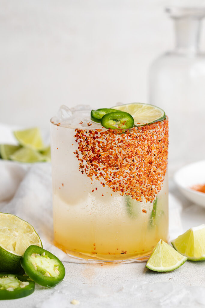 spicy margarita mocktail in a glass with fresh lime and jalapeno slices on the side.