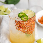 spicy margarita mocktail in a glass with a spicy tajin rim and a lime slice on top.