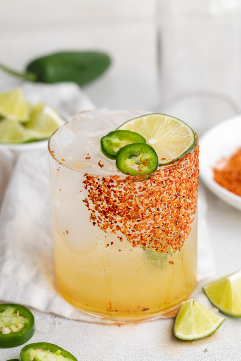 spicy margarita mocktail in a glass with a spicy tajin rim and a lime slice on top.