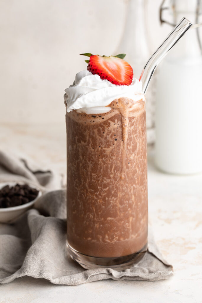 healthy milkshake in a glass with whipped cream and a strawberry on top.