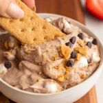 graham cracker being dipped into high protein s'mores dip.