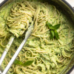 overhead image of protein pesto pasta in a skillet with fresh basil on top.