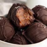 close up image of healthy no-bake brownie balls in a bowl, one with a bite taken out.