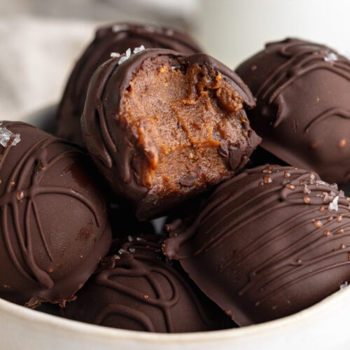 close up image of healthy no-bake brownie balls in a bowl, one with a bite taken out.