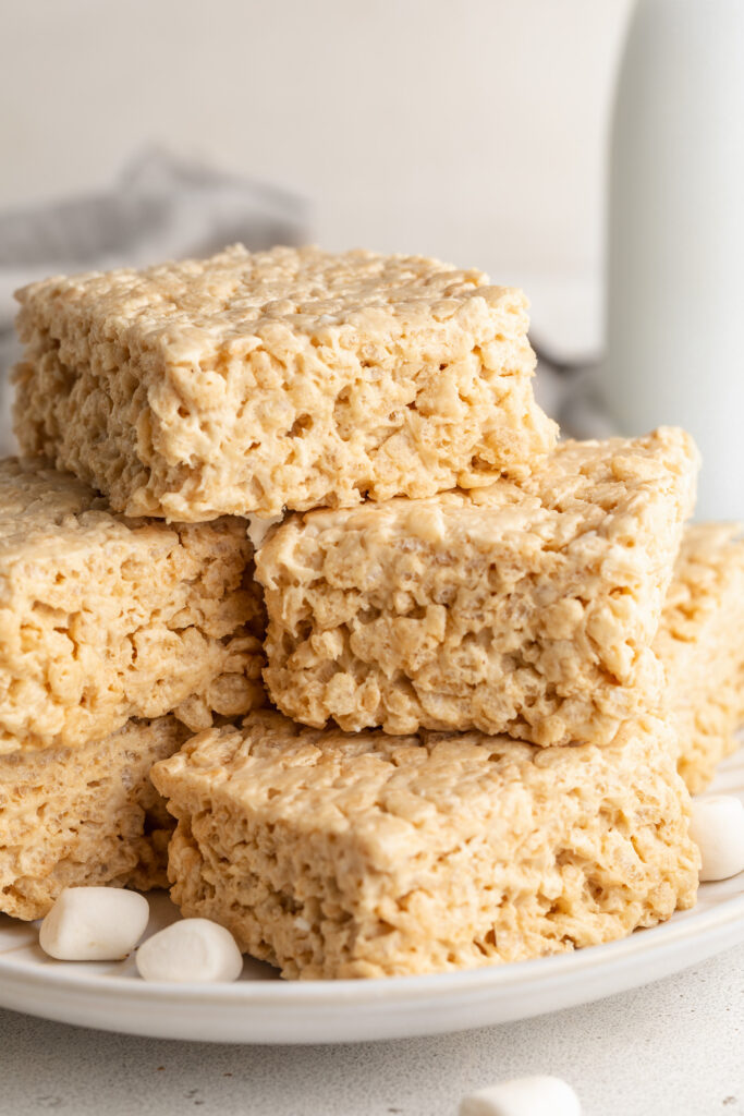 protein rice crispy treats stacked on a plate with mini marshmallows.