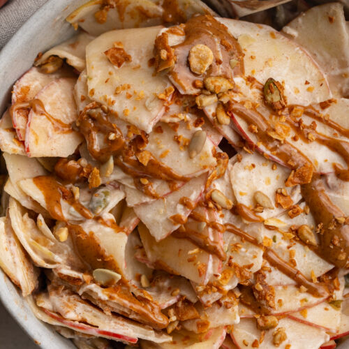 overhead image of healthy apple pie salad in a bowl with a drizzle of peanut butter and granola on top.