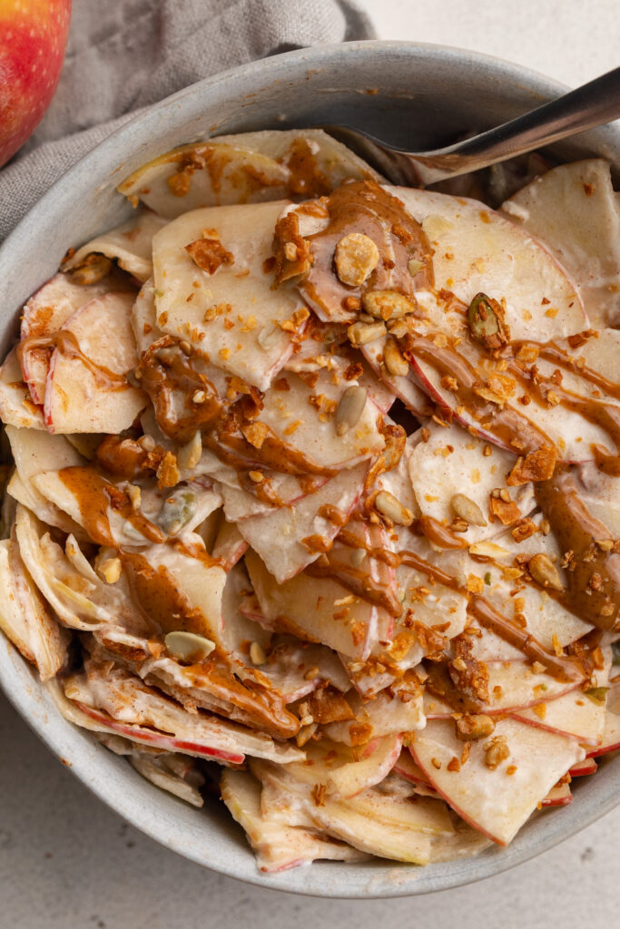 overhead image of healthy apple pie salad in a bowl with a drizzle of peanut butter and granola on top.