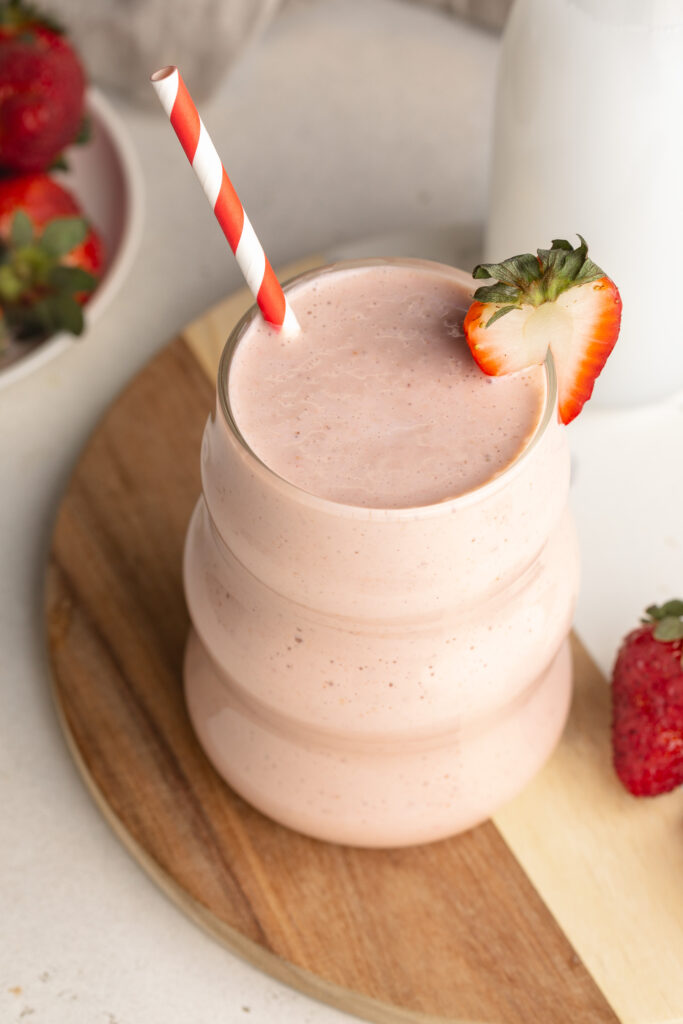 overhead image of cottage cheese smoothie with a straw and strawberry.