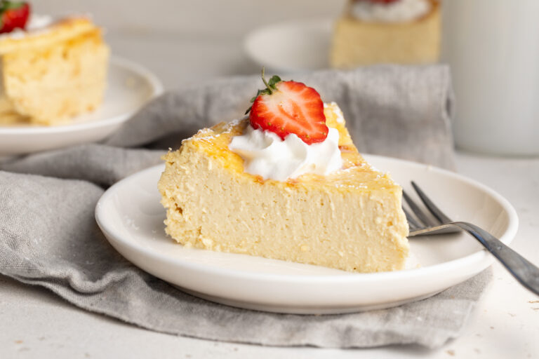5 ingredient healthy cheesecake slice on a plate with whipped cream and a strawberry on top.