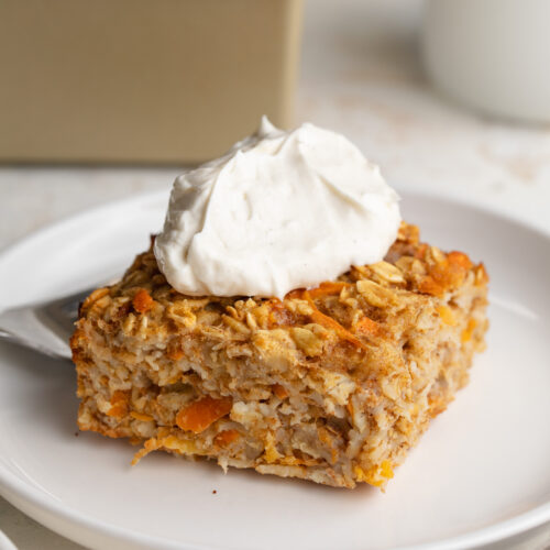 carrot cakes baked oats square on a plate with greek yogurt cream cheese frosting on top.