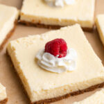 close up image of a cottage cheese cheesecake bar with whipped cream and a raspberry on top.