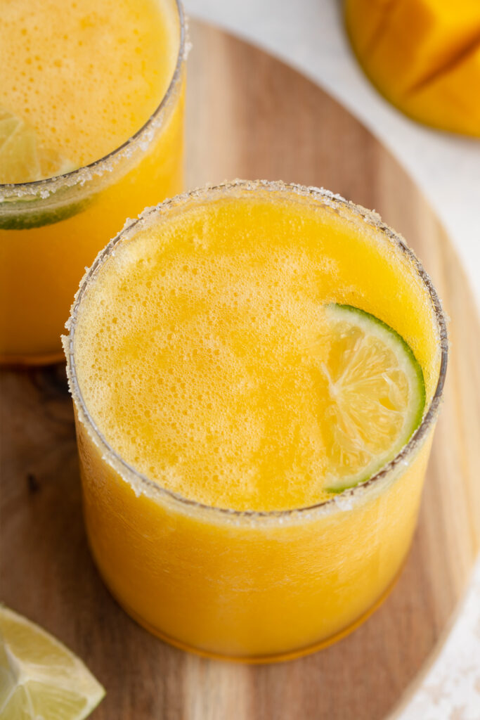 mango margaritas in a glass with a lime slice on top.