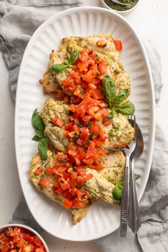 overhead image of pesto grilled chicken on a serving tray with bruschetta tomatoes on top.