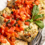 close up image of pesto grilled chicken on a plate with bruschetta tomatoes and fresh basil on top.