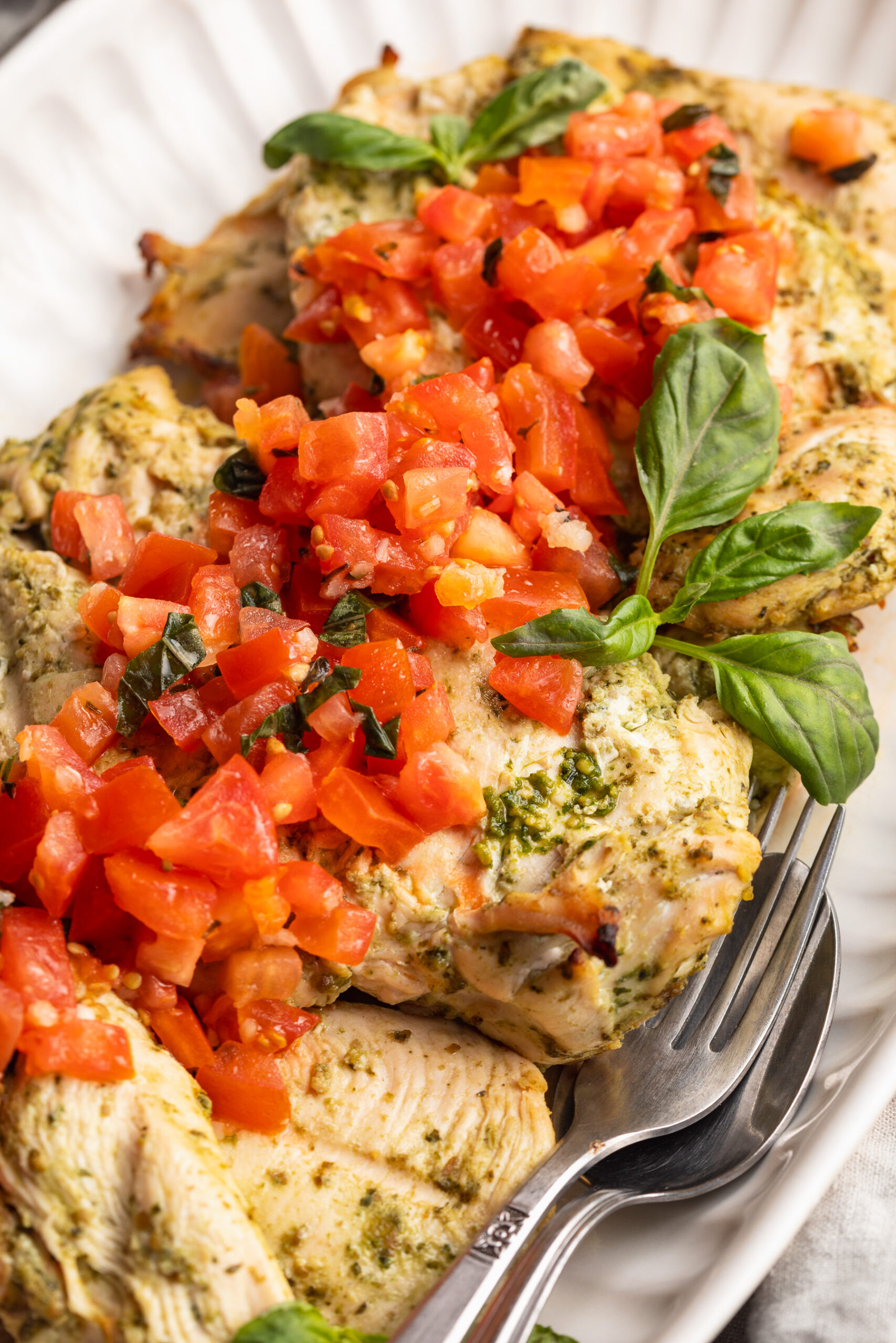close up image of pesto grilled chicken on a plate with bruschetta tomatoes and fresh basil on top.