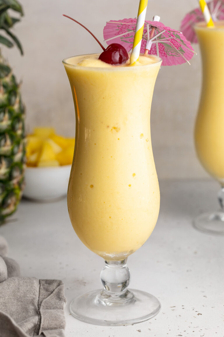 Easy 3-Ingredient Piña Colada Recipe (NO added sugar!) 3 ingredient pina colada in a glass with a cherry and umbrella on top.