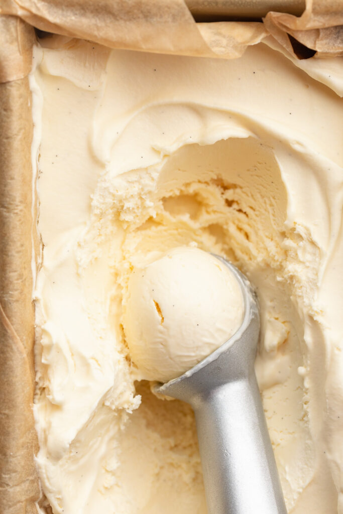 homemade vanilla bean ice cream in a container being scooped.