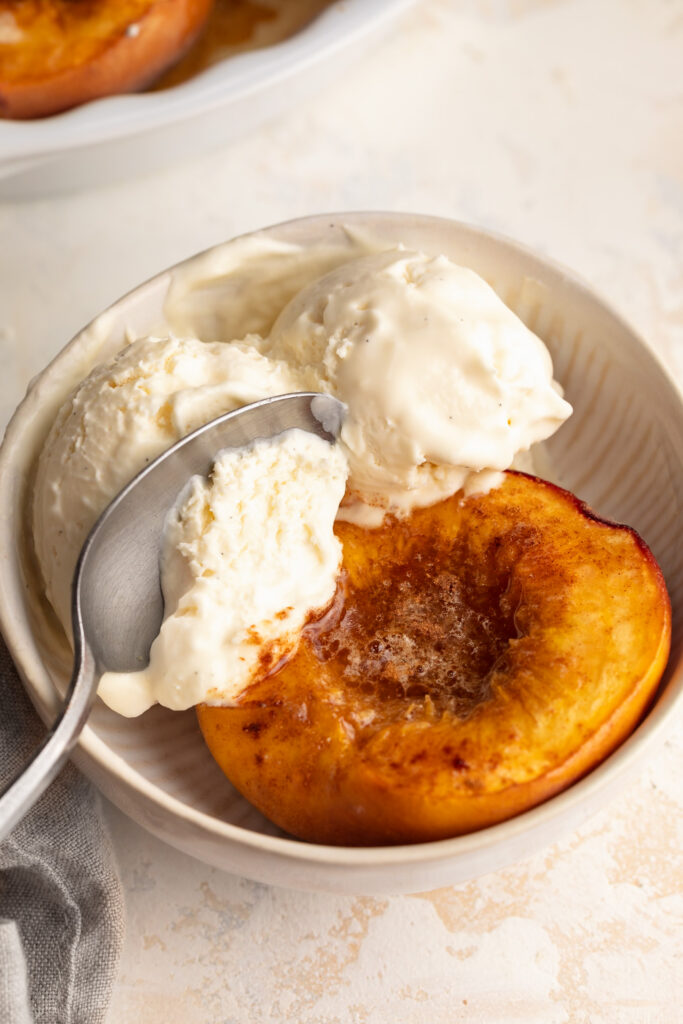 baked peach in a bowl with two scoops of homemade vanilla ice cream and a spoon.