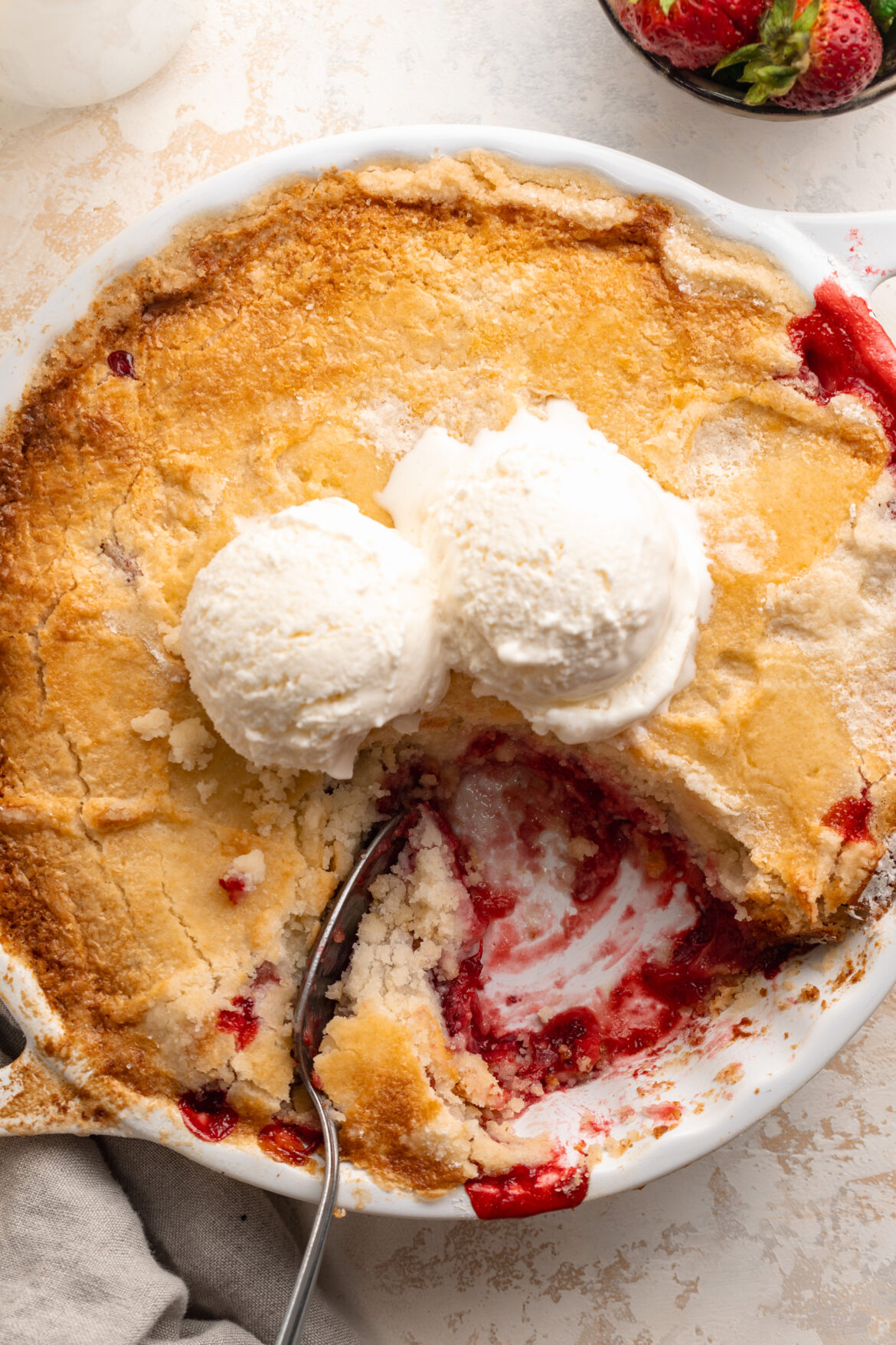 EASY 3-Ingredient Strawberry Dump Cake overhead image of 3 ingredient strawberry dump cake in a baking dish with ice cream on top.
