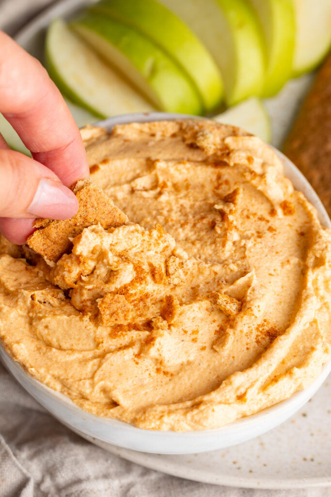 pumpkin protein cheesecake dip in a bowl being scooped by a graham cracker.