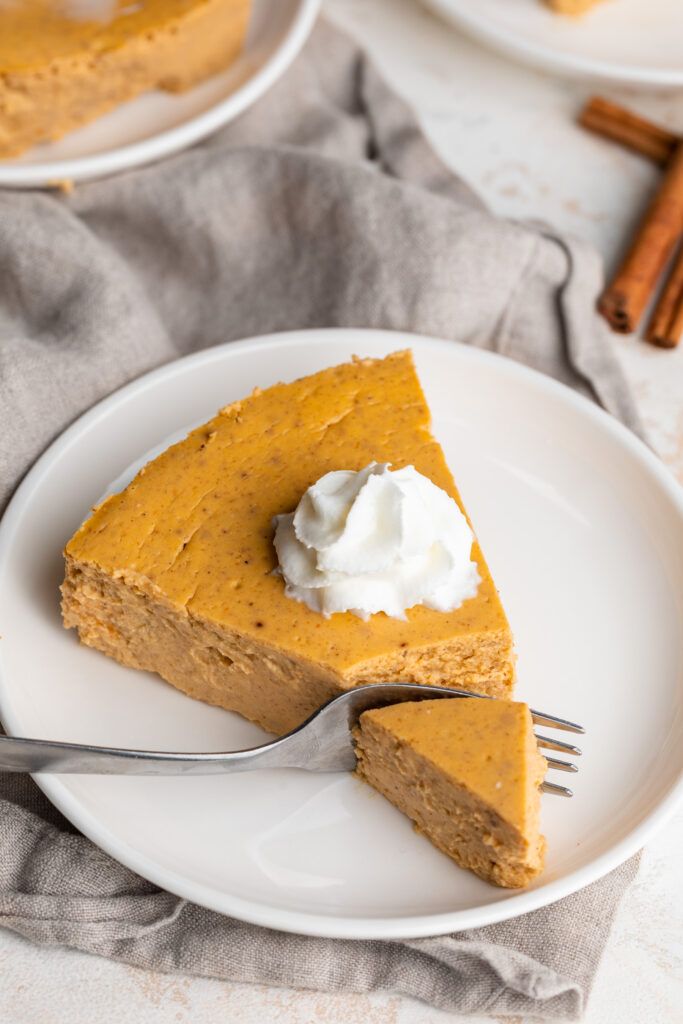 healthy pumpkin cheesecake slice on a plate with whipped cream on top being eaten with a fork.