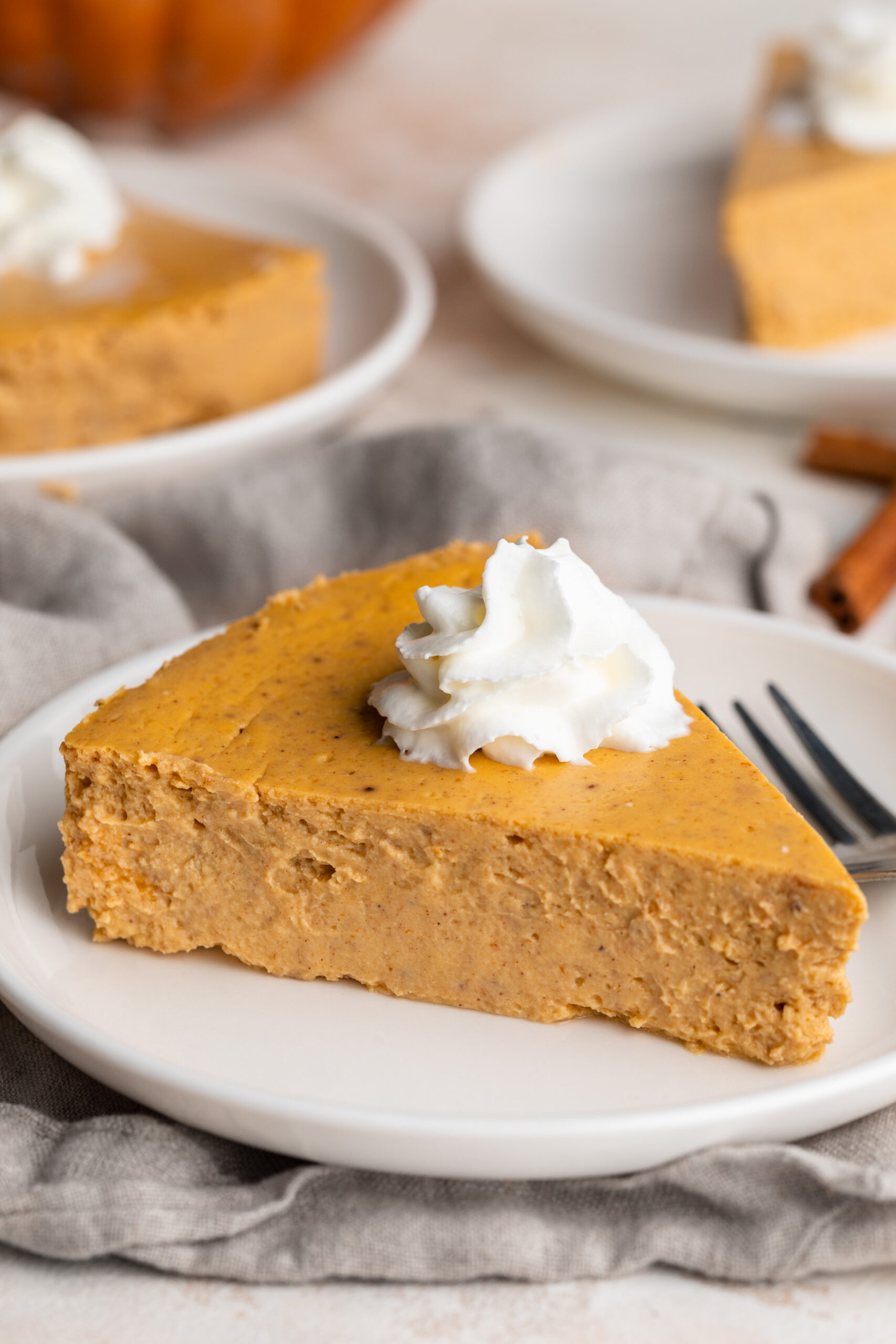 healthy pumpkin cheesecake slice on a plate with whipped cream on top.