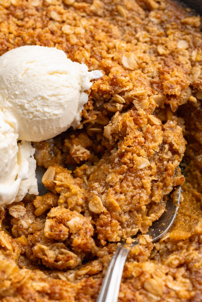 healthy pumpkin crisp being scooped out of a skillet with a spoon.