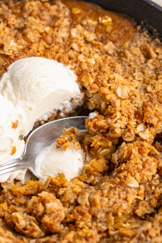 close up image of healthy pumpkin crisp in a cast iron skillet with ice cream on top.