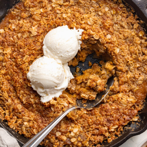 overhead image of healthy pumpkin crisp in a cast iron skillet with ice cream on top.