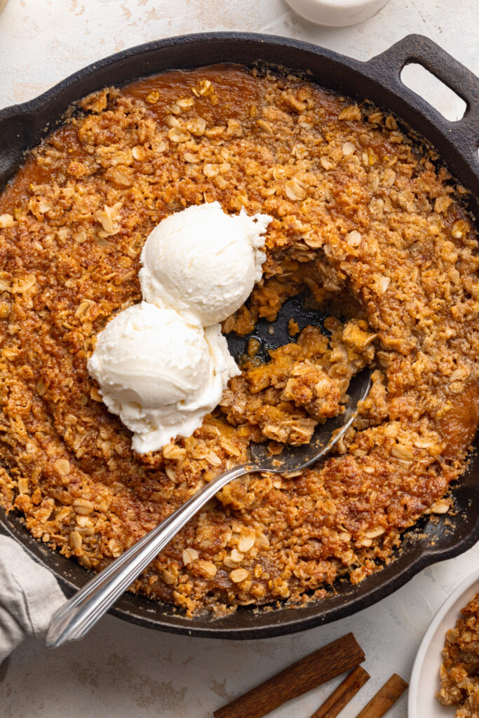 overhead image of healthy pumpkin crisp in a cast iron skillet with ice cream on top.